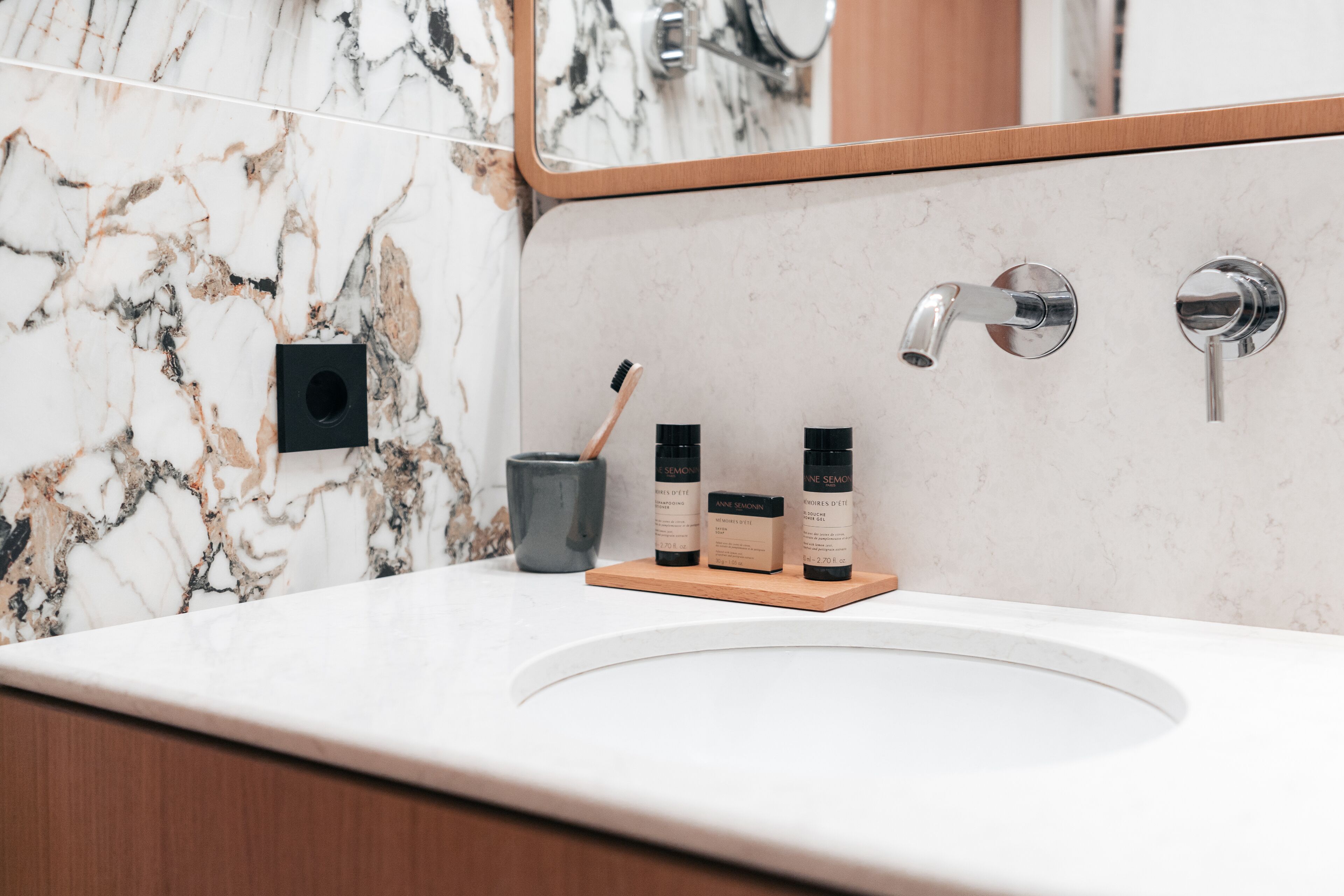 A bathroom with a marble backsplash, a sink with a wooden tray holding toiletries, and a mirror above the sink.