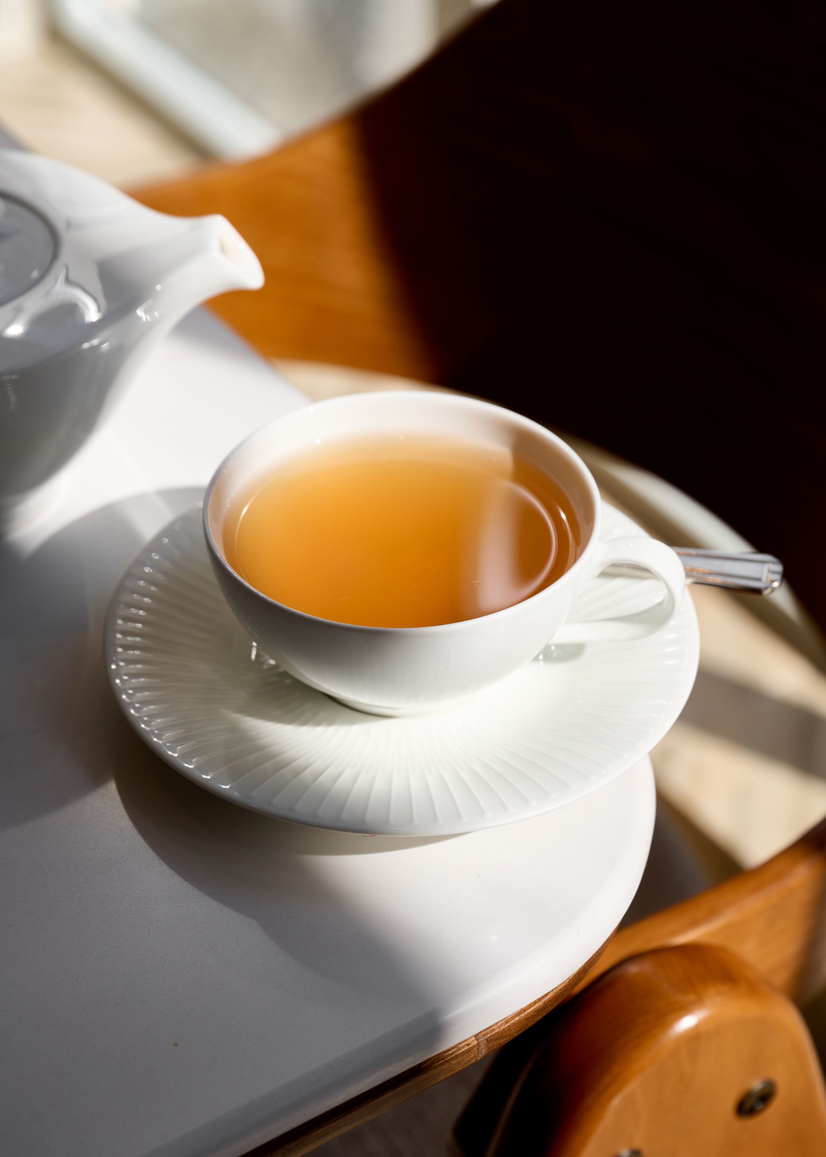Eine weiße Teetasse auf einem Untertasse, ein weißer Teekessel und ein Holztisch.