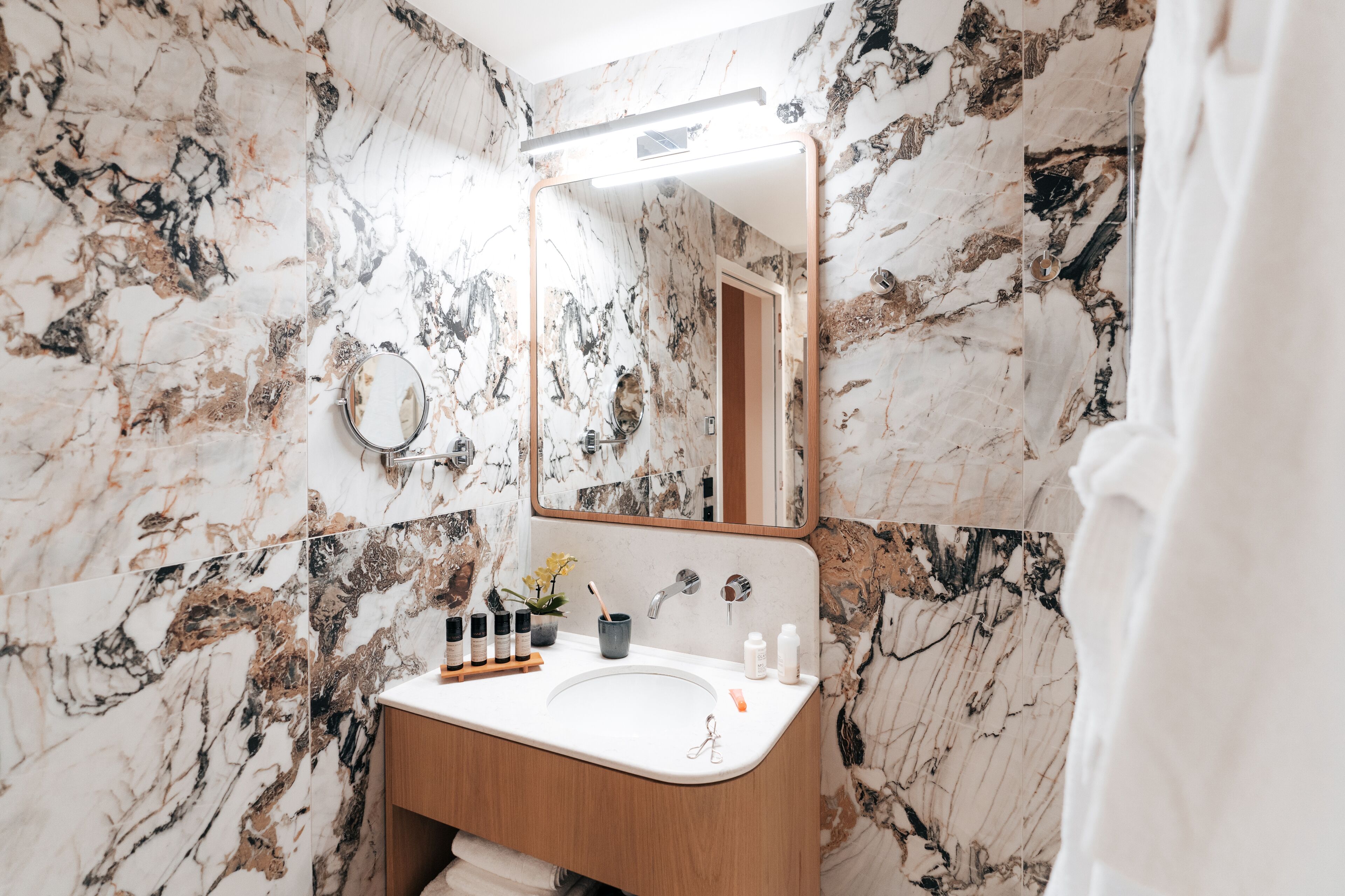 A bathroom with a marble wall, a wooden vanity, a sink, and a mirror.