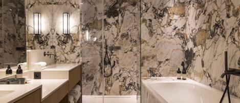 A modern bathroom with marble walls, a large bathtub, and a vanity with a mirror and lighting.