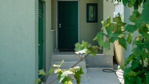 Un étroit sentier mène à une porte d’un vert foncé, avec une petite marche et un tableau encadré au-dessus.