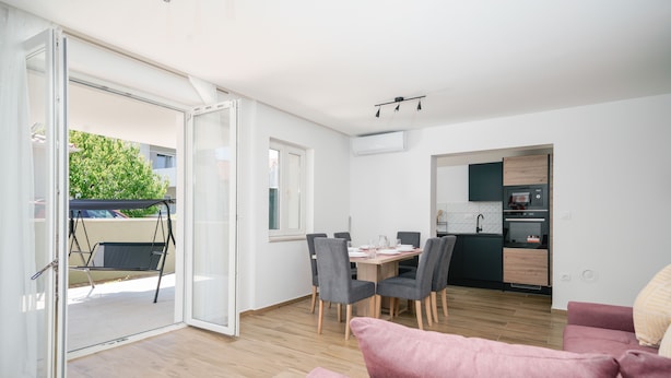 Un appartement moderne comprenant un coin repas, une cuisine et une porte-fenêtre coulissante donnant sur un espace extérieur aménagé pour se détendre.