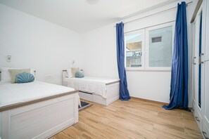 Quarto com cama, uma pequena escrivaninha, janela com cortinas e chão de madeira.