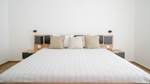 Un lit bien fait, recouvert d’une couvre-lit à rayures, deux tables de chevet avec des lampes et un mur sobre.