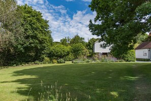 A well-maintained lawn with a white house and surrounding trees.