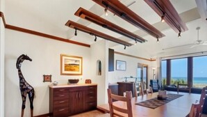 A spacious dining area with a long wooden table and chairs, a giraffe sculpture, and a view of the ocean through large windows. - Welcome to THE HIVE. A hub for peace and relaxation. DIRECT GULF views (Placida)