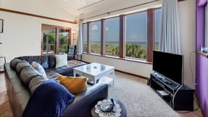 A living room with a large window, a ceiling fan, a sofa, a coffee table, and a TV. - Welcome to THE HIVE. A hub for peace and relaxation. DIRECT GULF views (Placida)