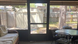 Uma sala de sol com vista para um quintal, incluindo uma área cercada e uma árvore.