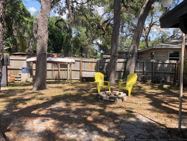 Un patio trasero con cerco de madera, dos sillas Adirondack amarillas y un área de patio techada.