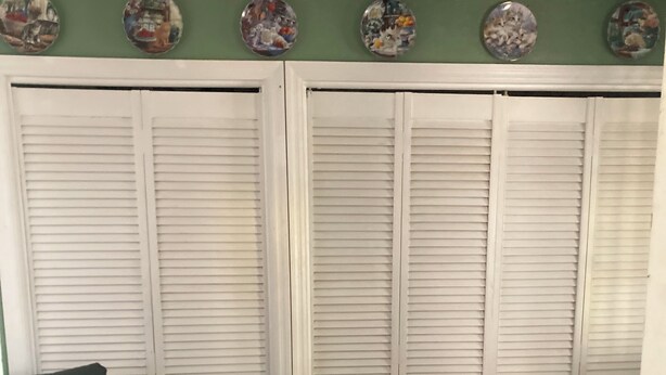Um quarto com parede verde, poltrona verde escura e armários brancos com venezianas.