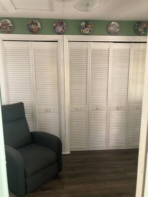 Una habitación con una pared verde, un sillón verde oscuro y armarios blancos con listones.
