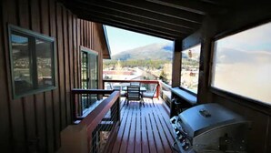 Eine Holzterrasse mit Grill und Sitzgelegenheit, mit Blick auf einen Fluss und Berge.