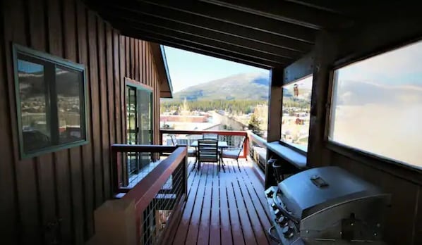 Eine Holzterrasse mit Grill und Sitzgelegenheit, mit Blick auf einen Fluss und Berge.