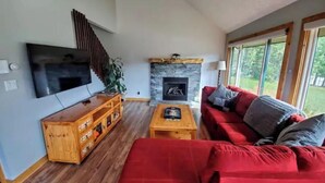 Ein Wohnzimmer mit Fernseher, einer Holz-Unterhaltungsecke, einem roten Sofa und einem Steinkamin.