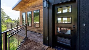Un bâtiment moderne en bois, doté d’une porte sombre, de grandes fenêtres et d’un balcon avec une rambarde en métal.