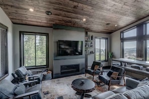 A modern living room with a fireplace, large windows, and a flat-screen TV.