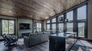 Une cuisine moderne dotée d’un grand îlot central, de planchers en bois foncé et de grandes fenêtres offrant une vue sur l’extérieur.