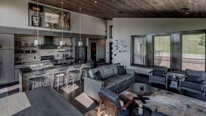 Une cuisine moderne avec un mur recouvert de pierres, un coin repas avec un canapé et des chaises gris, et une grande fenêtre avec des stores.