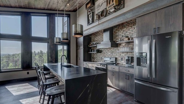 Une cuisine moderne dotée d’un grand îlot central, d’appareils électroménagers en acier inoxydable et d’un mur décoratif en briques.