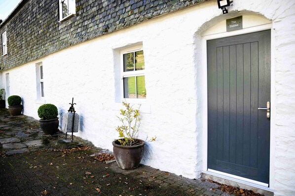 A white building with a dark door, a small window, and a potted plant. - The Stables -  Retreat Group (Pitlochry)