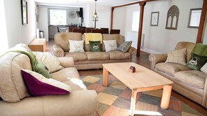 Een ruime woonkamer met een beige bank, een houten salontafel en een kamerkleed met dessin.