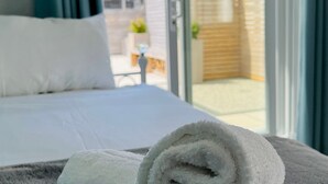 Una habitación de hotel con una cama, una toalla blanca enrollada y vistas al exterior a través de un ventanal.