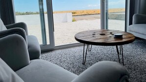 Un interior moderno con una zona de estar, una mesa redonda de madera y puertas de vidrio grandes que dan a un espacio exterior.