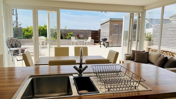 Una cocina moderna con una isla grande, un fregadero y una zona de barbacoa visible a través de puertas correderas de vidrio.