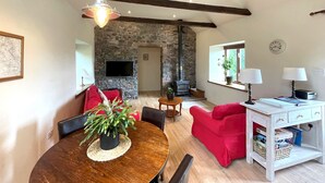 Una sala de estar acogedora con una pared de piedra, una chimenea, una mesa de comedor con sillas y un sofá rojo.