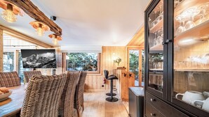 Interior acollidor d'una cabana amb zona de dinar, mobles de vimbles, un tamboret i un armari amb recipient de vidre.