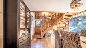 Una escala de fusta que condueix a una zona de menjador amb mobles de viquès i una paret de pedra al fons.