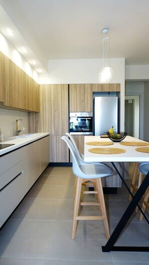 A modern kitchen with wooden cabinets, a built-in oven, and a dining area with a white table and chairs. - Luxurious, modern, cozy apartment in Heraklion (Heraklion)