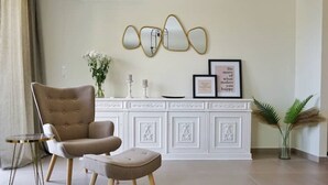 A living room with a tufted armchair, a small round table, a decorative cabinet, and a framed quote on the wall. - Luxurious, modern, cozy apartment in Heraklion (Heraklion)