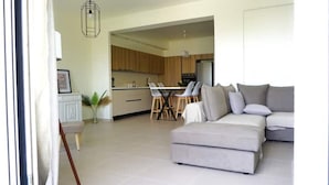 A modern living room with a grey sectional sofa, a dining area with a white table and chairs, and a kitchen with wooden cabinets. - Luxurious, modern, cozy apartment in Heraklion (Heraklion)