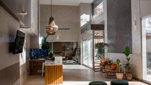 Eine geräumige Lobby mit einem Holzbüro, bequemen Sitzgelegenheiten, großen Fenstern und einer hängenden Leuchte.