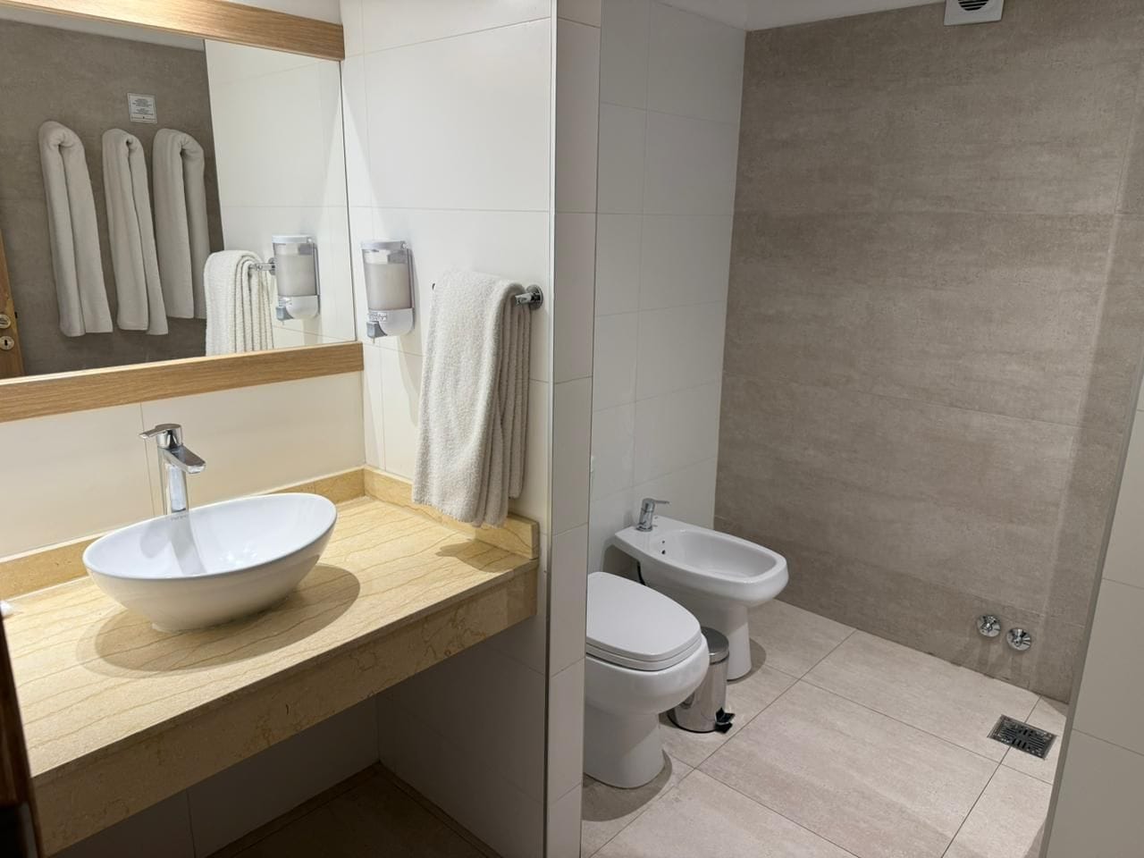 A modern bathroom with a large sink, two toilets, and a shower area.