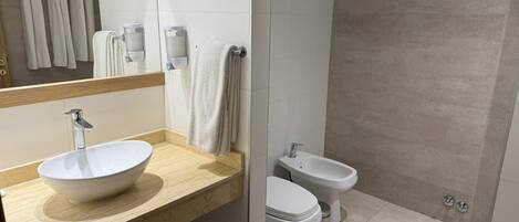 A modern bathroom with a large sink, two toilets, and a shower area.