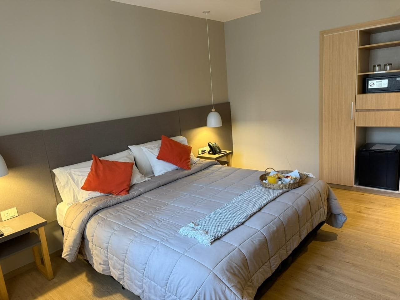 A hotel room with a bed, bedside table, lamp, and a minibar.