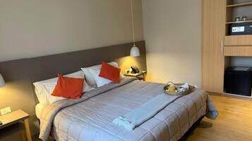 A hotel room with a bed, bedside table, lamp, and a minibar.