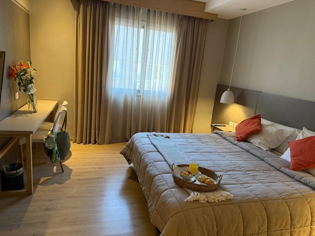 A hotel room with a bed, bedside table, lamp, and a window with curtains.