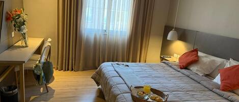 A hotel room with a bed, bedside table, lamp, and a window with curtains.