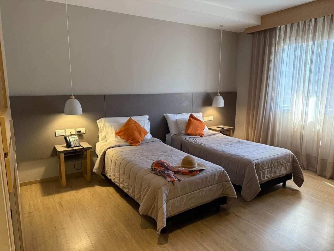 A hotel room with two beds, a bedside table with a phone, and a window with curtains.
