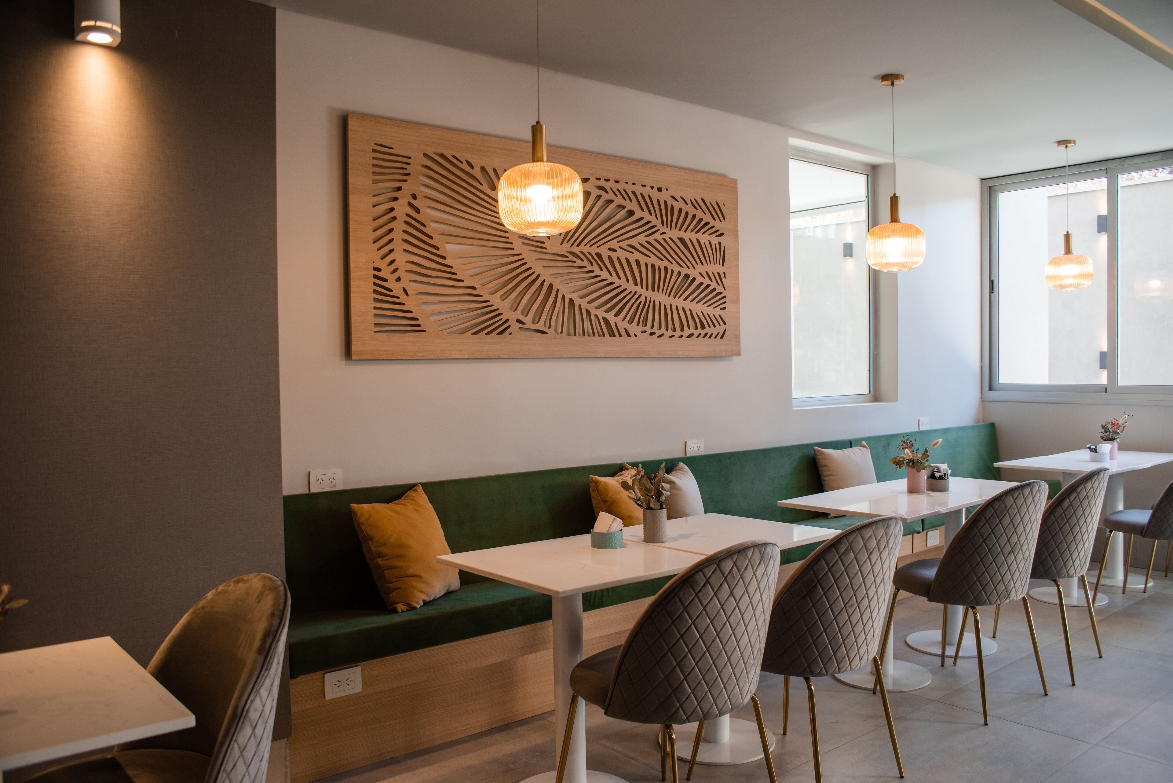 Interior de restaurante con una zona de asientos en cabinas verdes, mesas blancas y sillas grises.