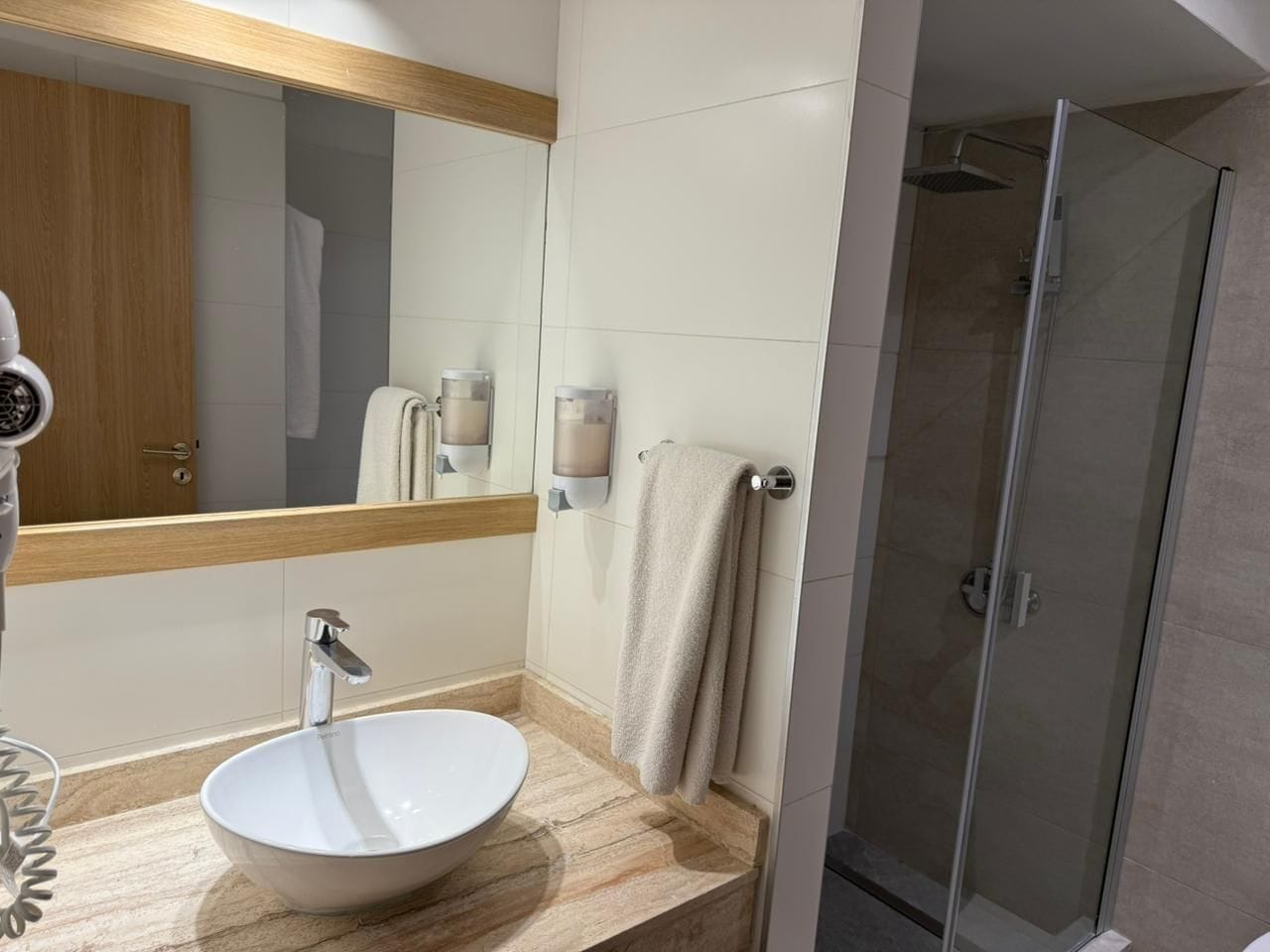 Een moderne badkamer met een rond wastafel, een spiegel, een handdoekrek en een douche met glazen wanden.