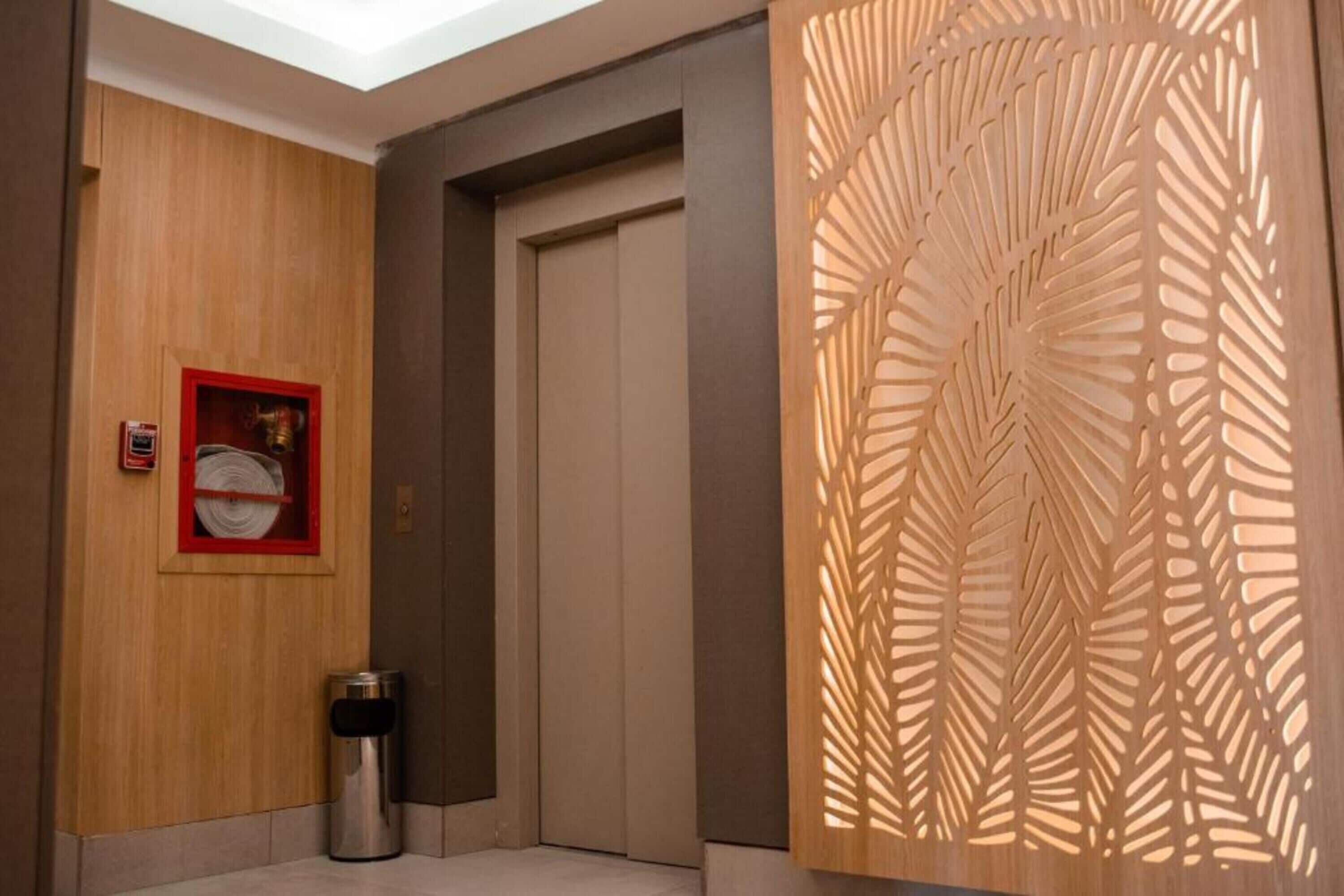 A hallway with a wooden wall, a door, a trash bin, and a decorative panel with leaf patterns.