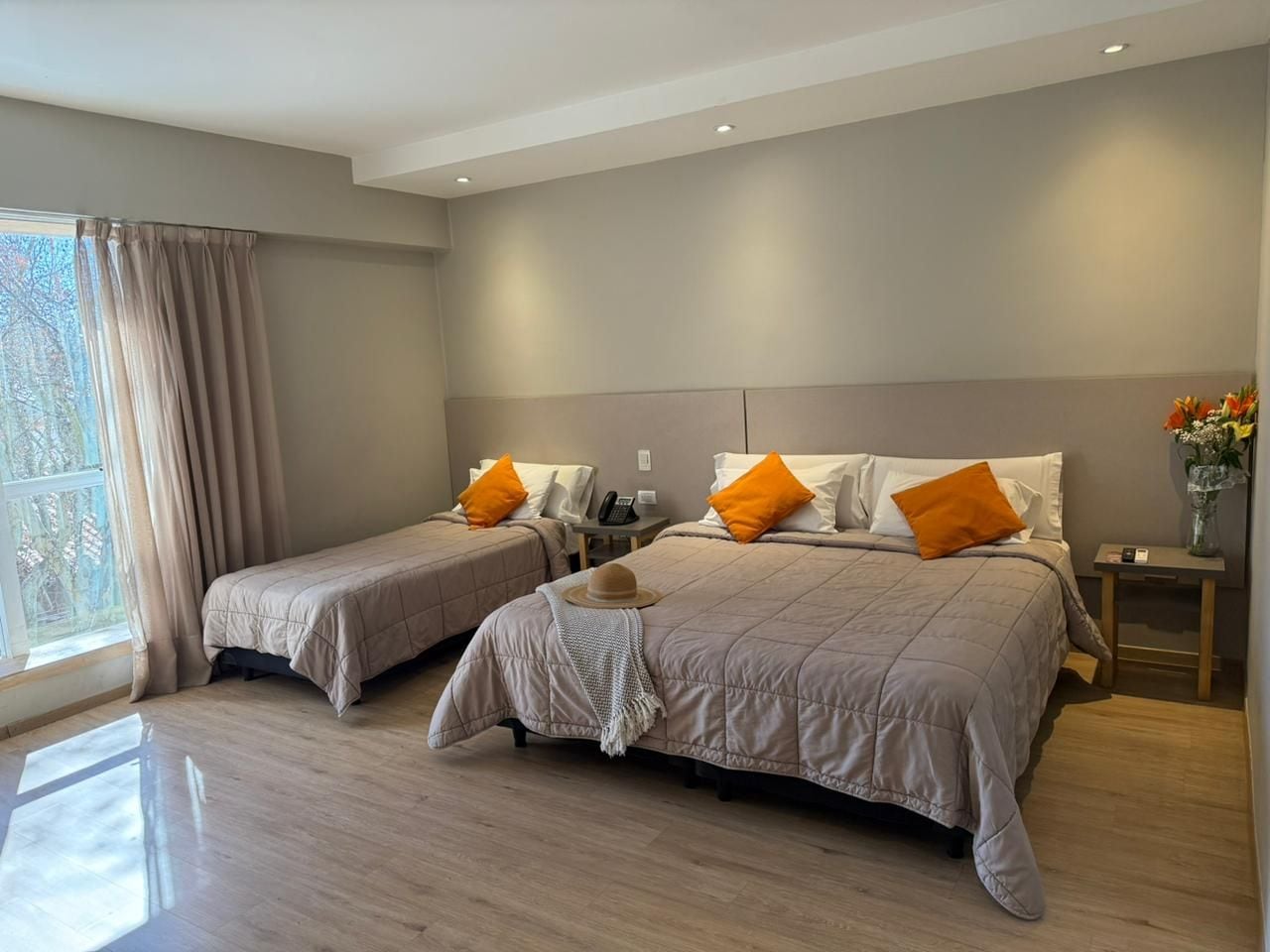 Habitació d'hotel amb dos llits, una finestra amb cortines, una taula de nit amb un telèfon i un vas amb flors.