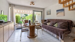 A cozy living area with a sofa, a dining table, and chairs. There is a sliding glass door leading to an outdoor area. - La Dunette - Two Bedroom Apartment, Sleeps 4 (La Grande-Motte)