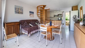 A compact living space with a dining area, a sofa, a wooden cabinet, and a kitchen in the background. - La Dunette - Two Bedroom Apartment, Sleeps 4 (La Grande-Motte)