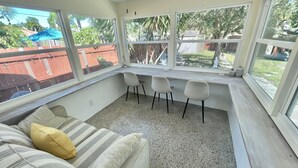 Une véranda avec un ventilateur de plafond, un banc près de la fenêtre avec des fauteuils, un canapé à rayures et une vue sur le jardin arrière.