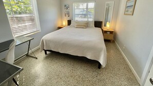 Une chambre à coucher avec un lit, un ventilateur de plafond, un bureau et une fenêtre avec des stores.
